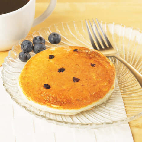 Delicious protein pancakes with blueberries on a clear plate next to a cup of coffee.